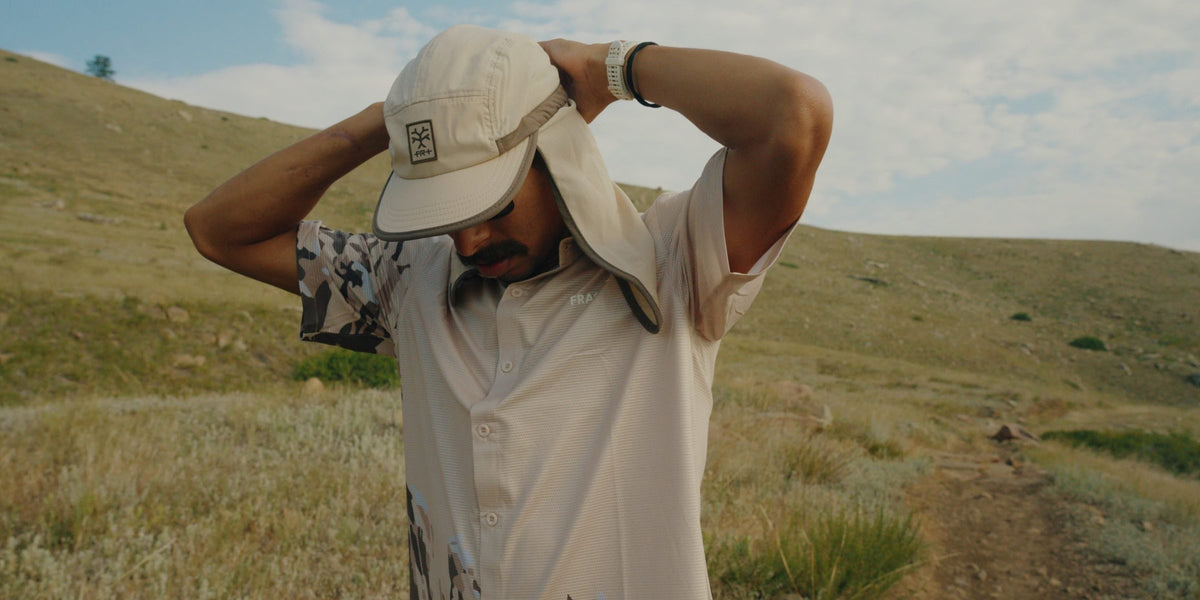 Runner in a cream Fractel legionnaire hat and shirt from the Rockies running collection on a grassy hillside