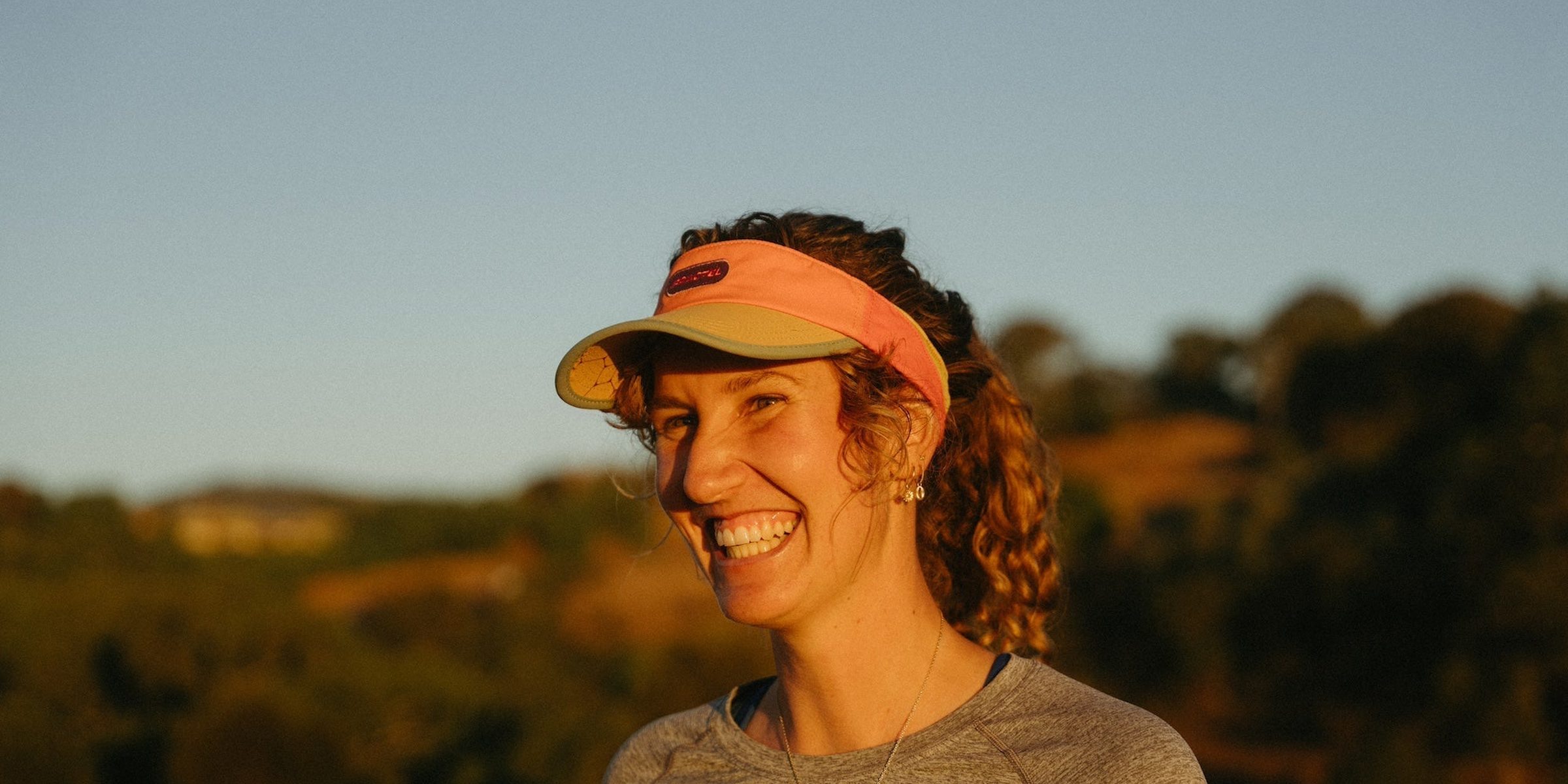 Smiling runner in an orange Fractel running visor in warm evening light