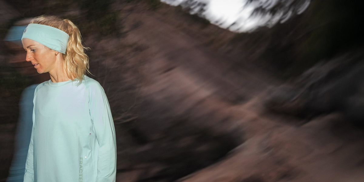Runner in a mint Fractel running headband and matching long sleeve top on a blurred trail