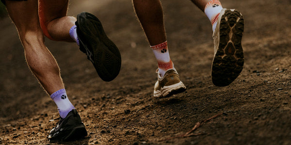 Trail runners' legs in patterned Fractel compression socks on a dirt track