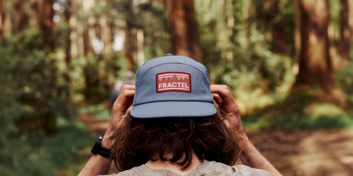 Runner adjusting a blue Fractel cap with a red patch in a forest, Memorial Day sale