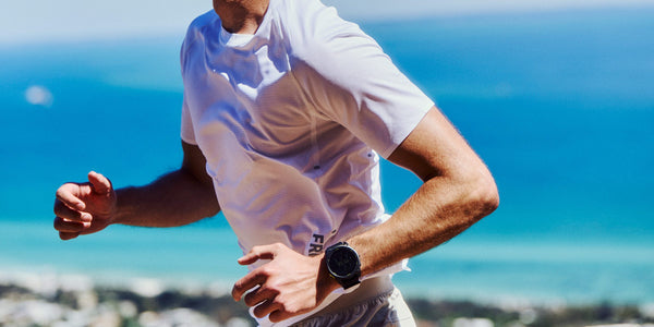 Man in a white Fractel tee from our mens running shirts range, mid-stride above the ocean