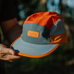 Orange and blue cap held by a person with a blurred natural background