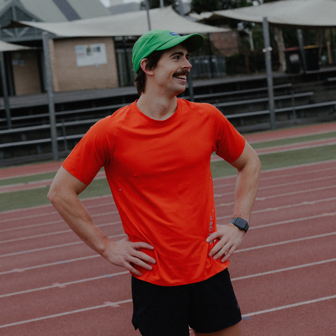 Male wearing an orange shirt and green cap on a track