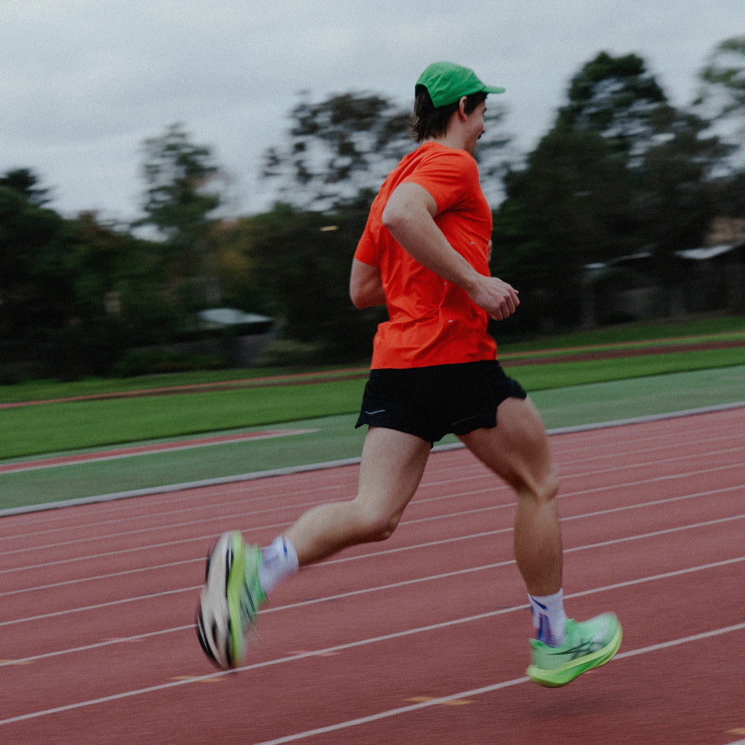 Male running on a track wearing an orange shirt and green cap