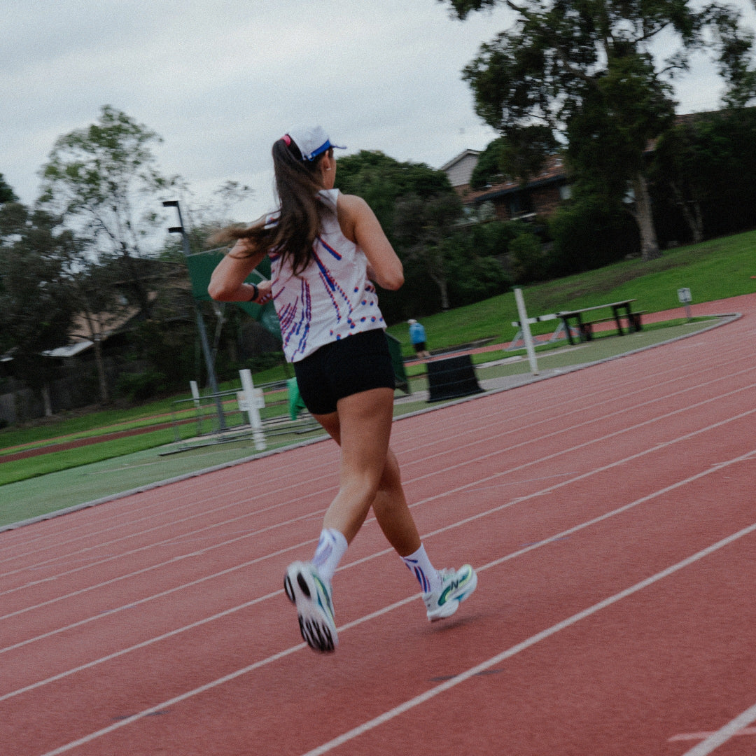 Women running on a track in white performance singlet