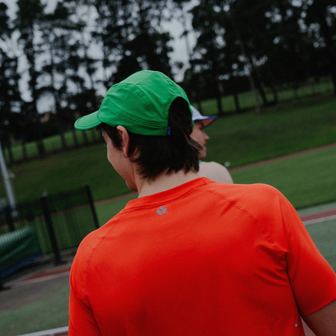Male wearing a green cap and orange shirt at a track